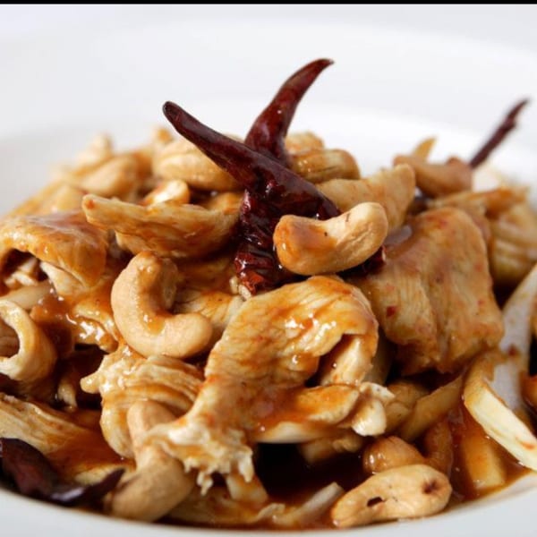Thai cashew chicken with dried red chilies and a savory sauce in a white bowl.