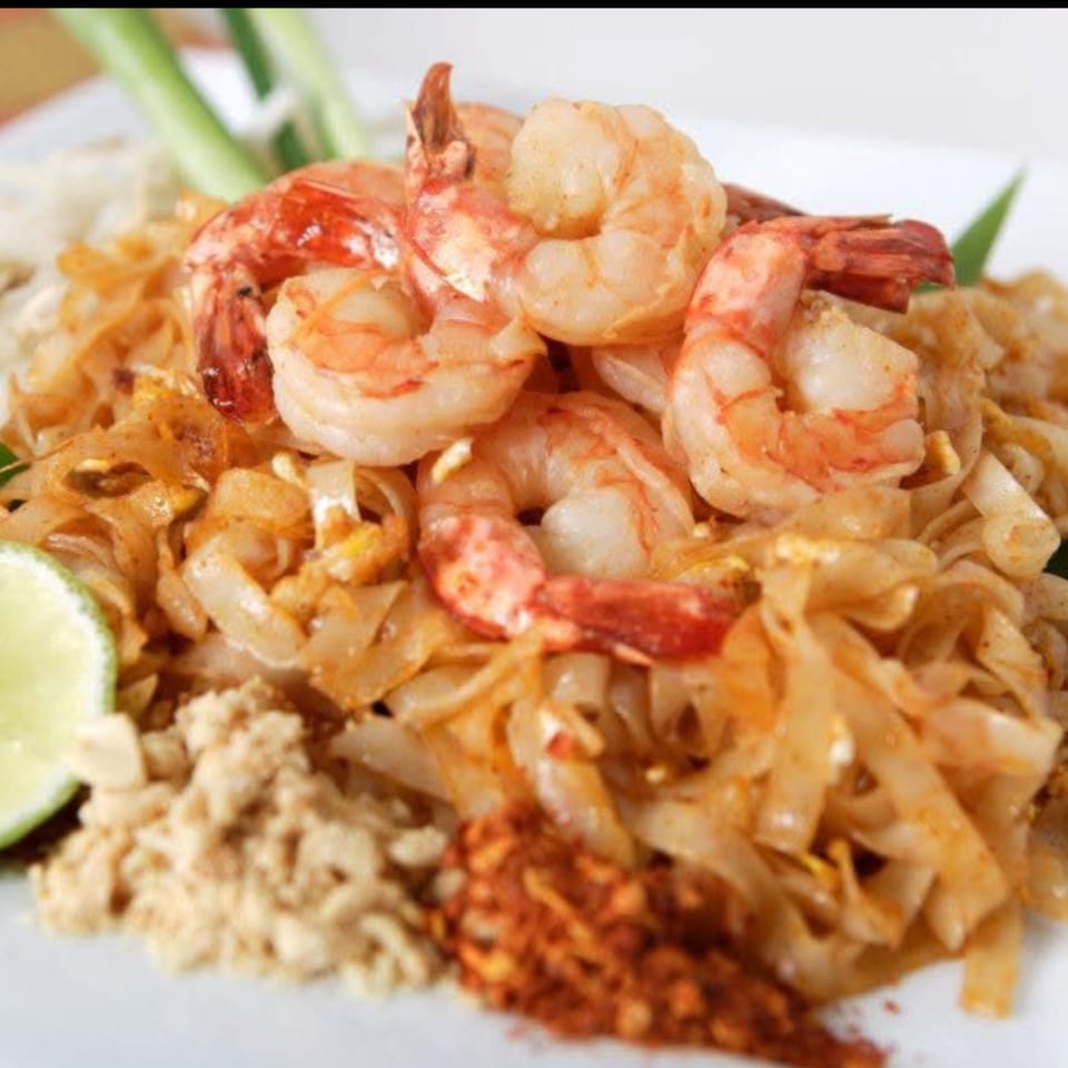 Close-up of Thai shrimp Pad See Ew with lime, crushed peanuts, and chili flakes.