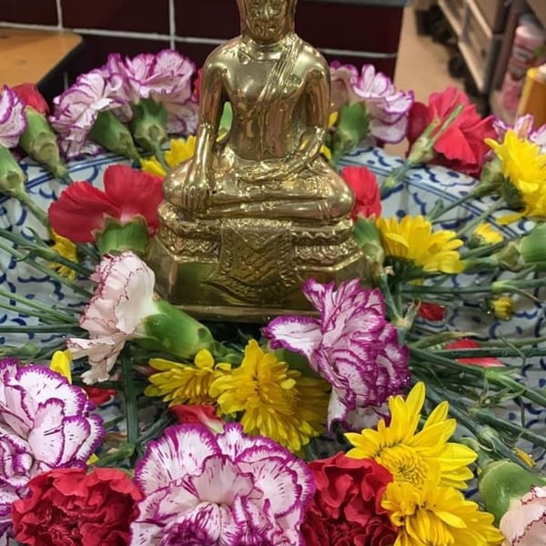 Golden Buddha statue surrounded by colorful red, purple, and yellow flowers in a decorative bowl.