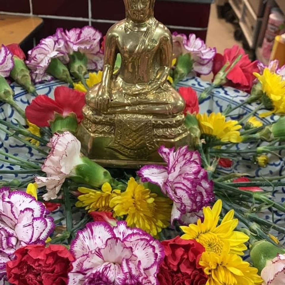 Golden Buddha statue surrounded by colorful red, purple, and yellow flowers in a decorative bowl.