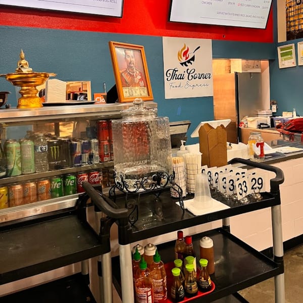 Interior of Thai Corner Food Express, showing a drink cooler, condiment cart, and Thai decor.