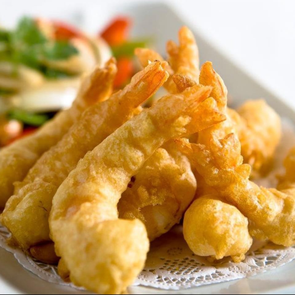 Golden-brown fried shrimp tempura, served on a white plate with a doily and a blurred salad.