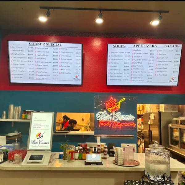 Thai Corner Food Express counter with menu boards, a neon sign, and self-order kiosks.